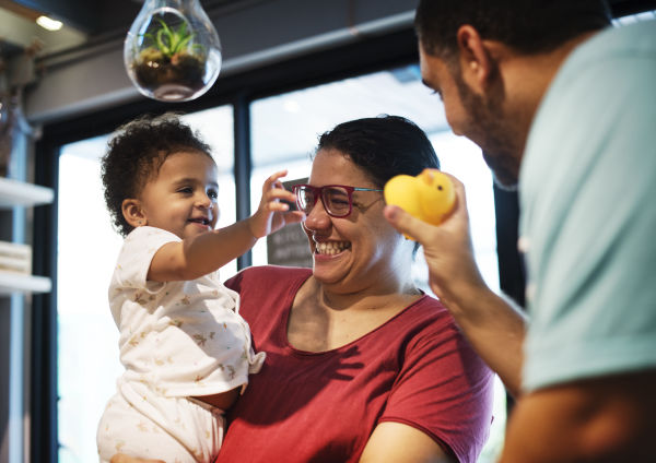 Toddler in grandmother's arms reaching out to toy held by other adult